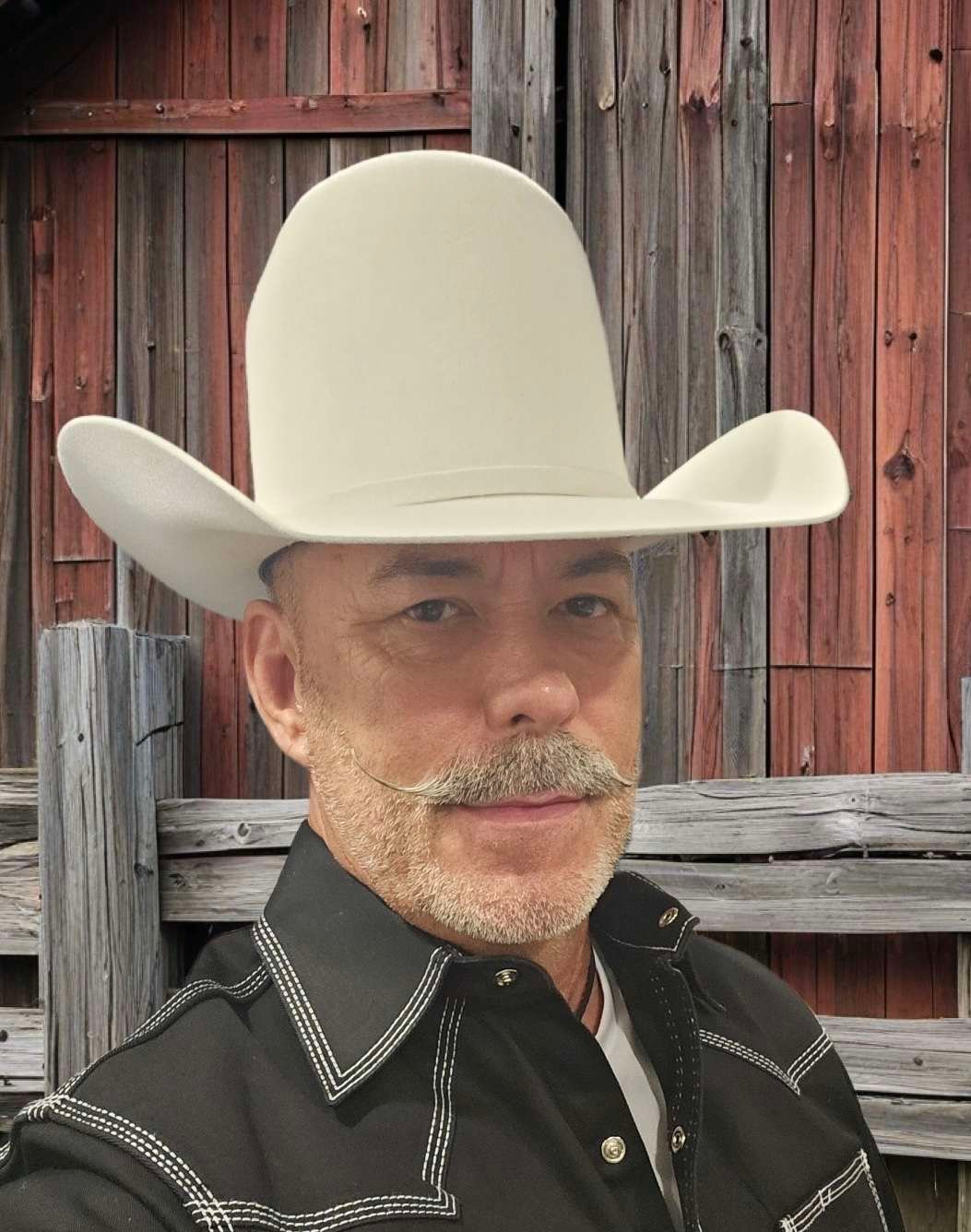 Man with cowboy hat and mustache by barn.
